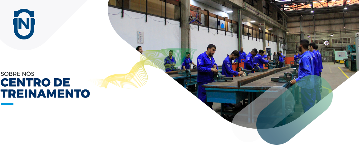 Imagem de cabeçalho de página do centro de treinamento. A imagem mostra vários funcionários realizando treinamento com equipamentos em cima de uma grande bancada. O ambiente de fundo é um galpão de fábrica.