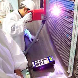 Imagem da galeria de imagem da página Sala Limpa. A imagem mostra 2 funcionários testando um equipamento de soldagem, junto a um gradil.