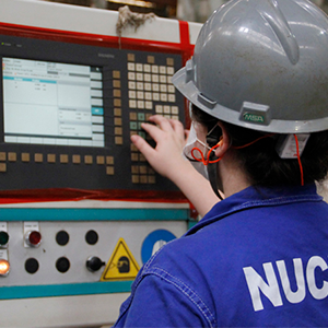 Imagem da galeria de imagem da página de Energia. A imagem mostra uma funcionária configurando um equipamento. A funcionária está de costas e veste jaleco e um capacete de proteção.
